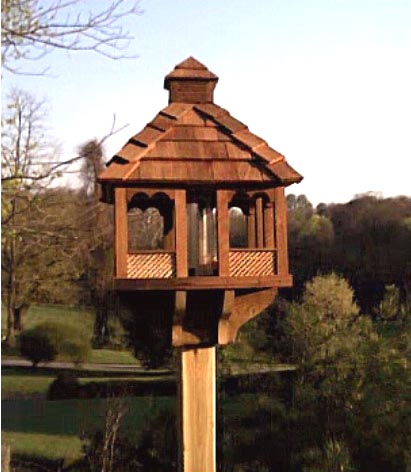 A hand crafted bird feeder on a red cedar post